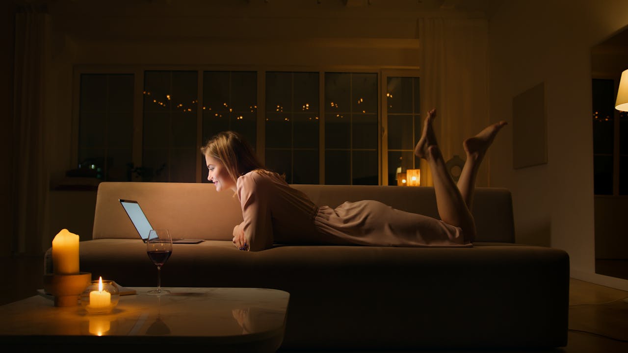 about-03 Caucasian woman smiling and relaxing on a sofa with a laptop at night.